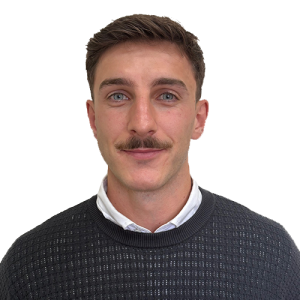 Portrait of a man with short brown hair and a mustache, wearing a dark knitted sweater over a white collared shirt, against a white background.